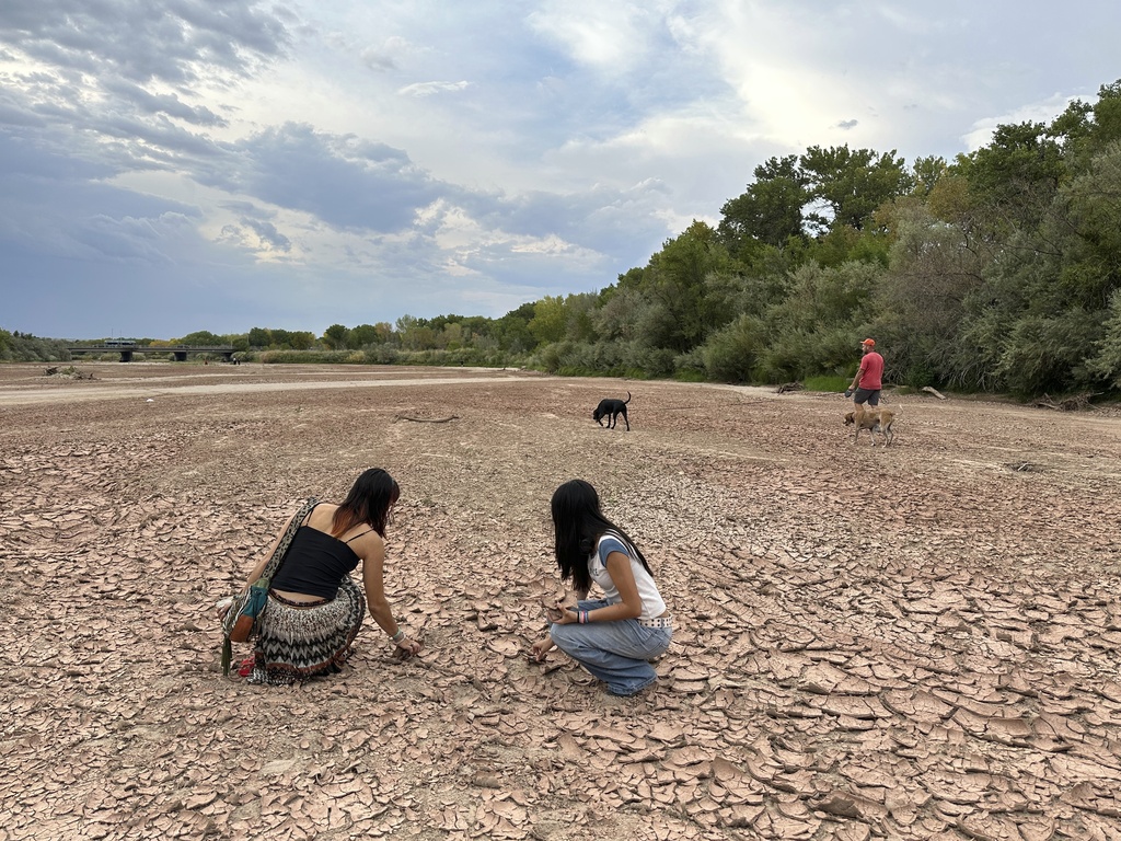Sisters Zoe Hughes, left, and Phoebe Hughes, center, collect pieces of clay from the Rio Grande as a man walks his dogs in the dry riverbed in Albuquerque, N.M., on Thursday, Aug. 21, 2025. (AP Photo/Susan Montoya Bryan)
