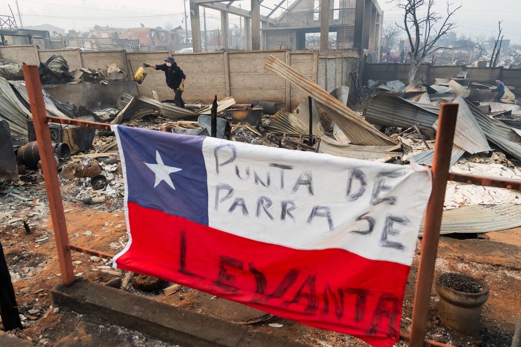A Chilean flag is covered by the Spanish message: "Punta Arenas rises" at a home destroyed by wildfires in Tome, Chile, Monday, Jan. 19, 2026. (AP Photo/Javier Torres)