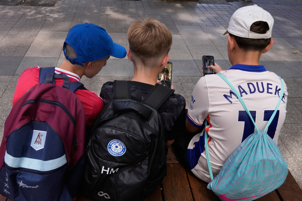 Hugo Winwood-Smith, right, Hardy Macpherson and Edan Abou, left, all 11-years-old, use their phones while sitting outside a school in Sydney, Monday, Dec. 8, 2025. (AP Photo/Rick Rycroft)