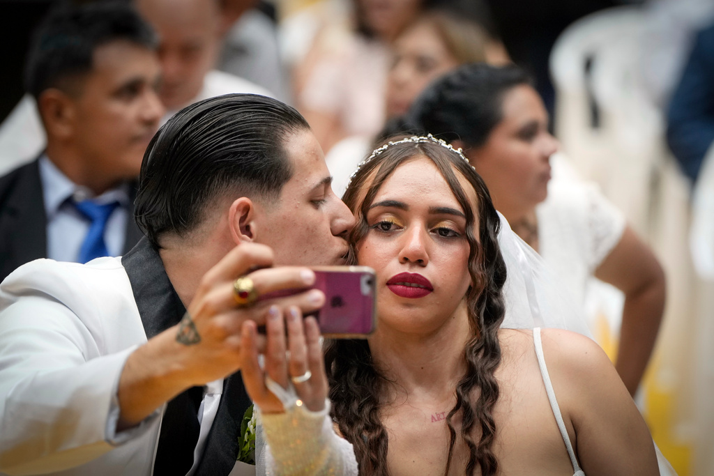 Jonathan Garay, left, and Fiorella Riveros take a selfie during a group wedding ceremony organized by the Civil Registry to legally formalize their unions in in Asuncion, Paraguay, Saturday, Oct. 4, 2025. (AP Photo/Jorge Saenz)