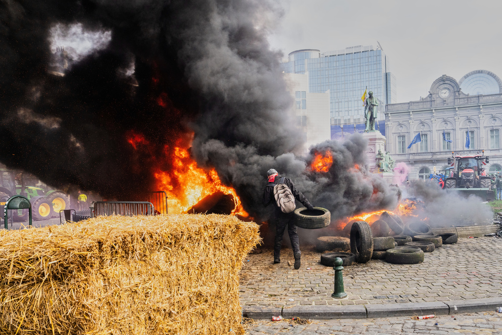 A protestor picks up tire to throw onto a fire during a demonstration of European farmers outside the EU Summit meeting in Brussels, Thursday, Dec. 18, 2025. (AP Photo/Marius Burgelman)