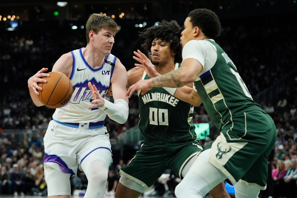 Utah Jazz's Kyle Filipowski, left, drives to the basket against Milwaukee Bucks' Jericho Sims (00) and Ryan Rollins, right, during the first half of an NBA basketball game Saturday, March 7, 2026, in Milwaukee. (AP Photo/Aaron Gash)