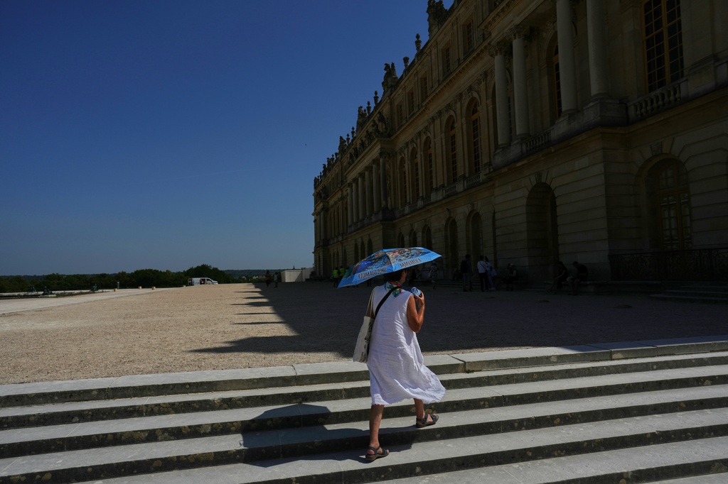 A woman shields herself from the sun with an umbrella as she walks in the garden of the Palace of Versailles, outside Paris, Monday, June 22, 2026. (AP Photo/Thibault Camus)