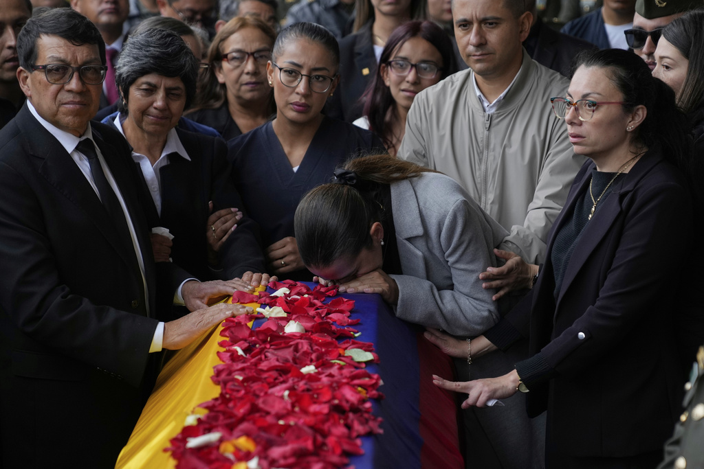 Police Maj. Adriana Pinzon kisses the coffin of her husband, Capt. Francisco Merchan, a police pilot killed when his helicopter was shot down by a dissident faction of the former FARC guerrilla group, as his father, Bernardo Merchan, and other relatives stand nearby during his burial in Mongua, Colombia, Monday, Aug. 25, 2025. (AP Photo/Fernando Vergara)