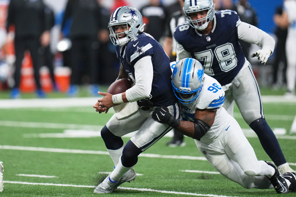 Dallas Cowboys quarterback Dak Prescott, left, tries to hold on to the ball as Detroit Lions defensive end Al-Quadin Muhammad (96) makes a hit during the second half of an NFL football game Thursday, Dec. 4, 2025, in Detroit. (AP Photo/Paul Sancya)