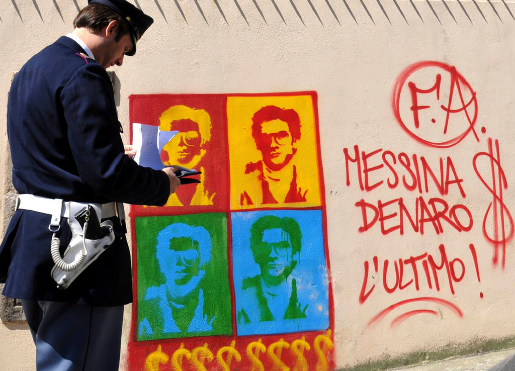 FILE - An Italian Police officer looks on at graffiti on the perimeter wall of Palermo's city's cathedral, portraying Matteo Messina Denaro, in Sicily, southern Italy, Thursday, April 24, 2008. (AP Photo/Alessandro Fucarini, File)