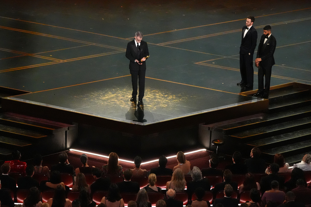 Paul Thomas Anderson accepts the award for writing (adapted screenplay) for "One Battle After Another" during the Oscars on Sunday, March 15, 2026, at the Dolby Theatre in Los Angeles. Chris Evans, second right, and Robert Downey Jr. look on from right.(AP Photo/Chris Pizzello)