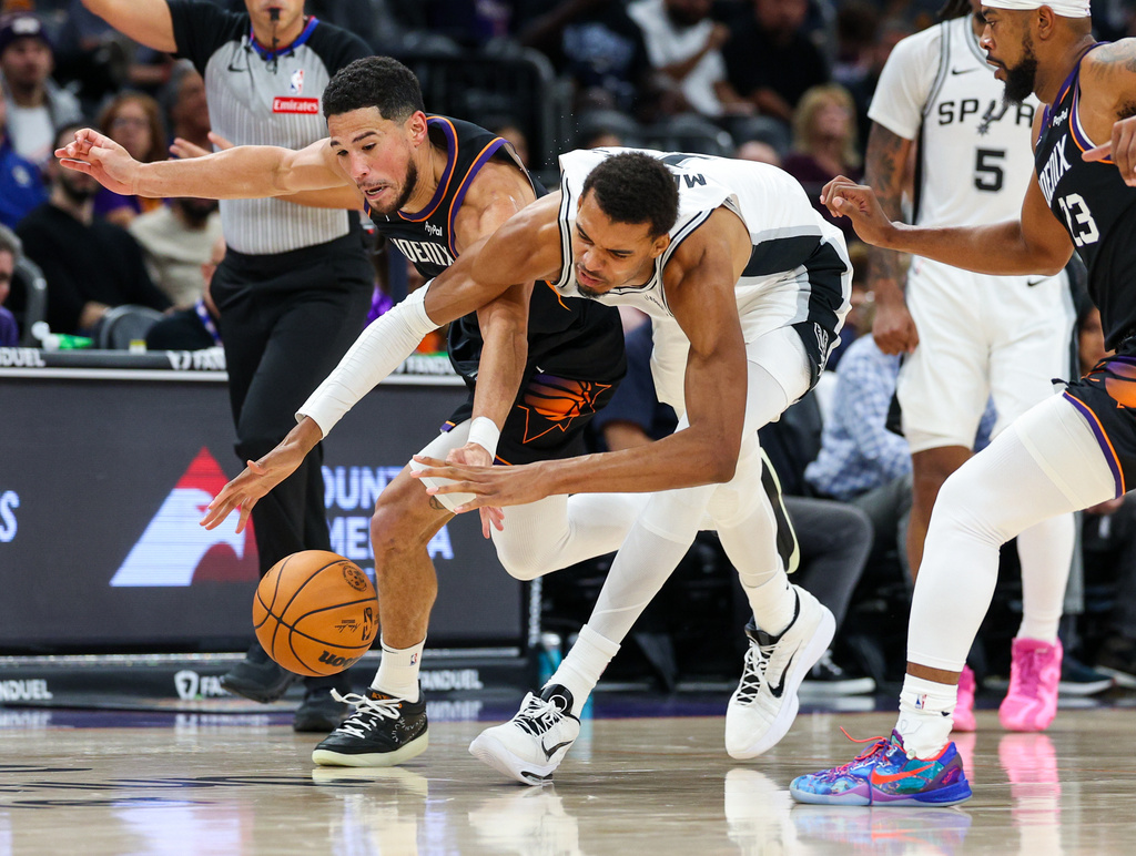 Phoenix Suns guard Devin Booker, left, and San Antonio Spurs forward Victor Wembanyama, second from left, battle for the ball during the first half of an NBA basketball game, Sunday, Nov 2, 2025, in Phoenix. (AP Photo/Mike Christy)