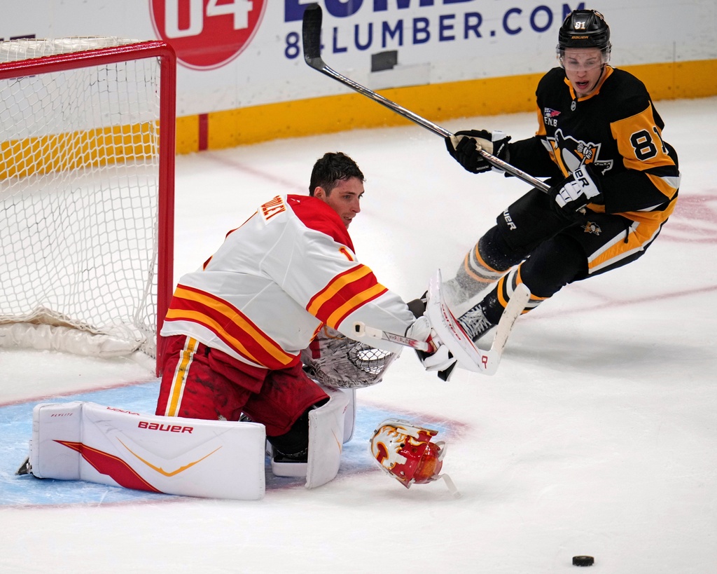 Calgary Flames goaltender Devin Cooley has his mask knocked off by a shot on goal with Pittsburgh Penguins' Ben Kindel (81) unable to get to the rebound during the first period of an NHL hockey game in Pittsburgh, Saturday, Jan. 10, 2026. (AP Photo/Gene J. Puskar)