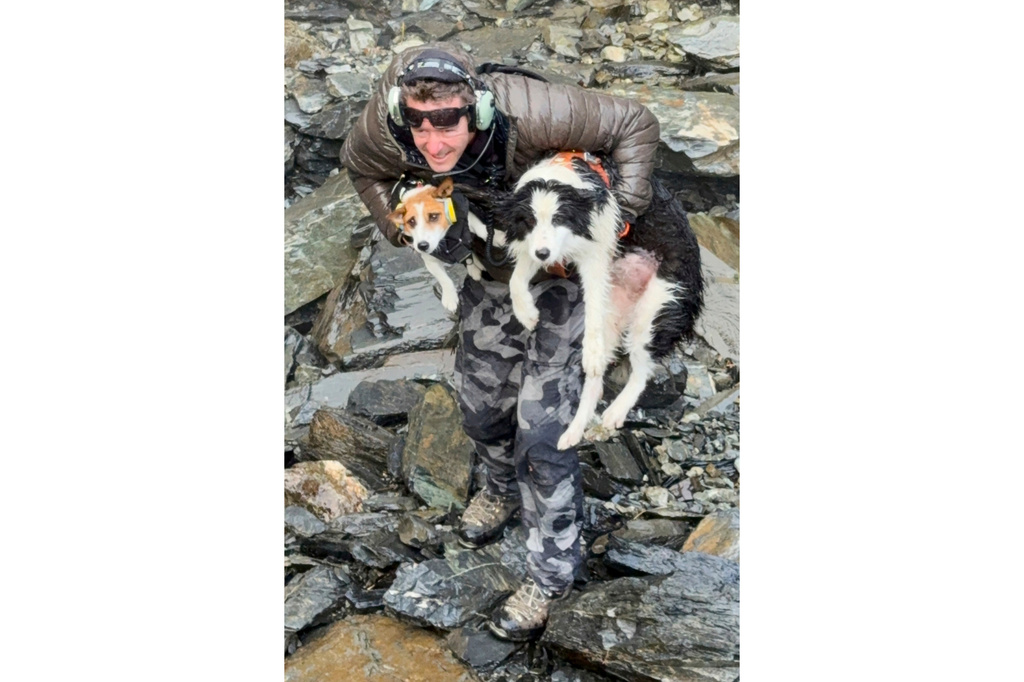 In this photo released by Precision Helicopters Ltd, Wayne Holmes holds his dog Bingo, left, after the rescue of Molly, right, at a waterfall on the Arahura River on the West Coast of the South Island of New Zealand, Tuesday, March 31, 2026. (Precision Helicopters Ltd via AP)