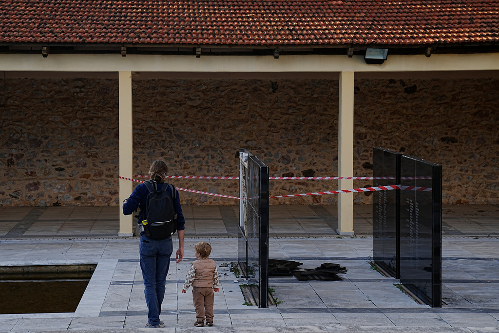 A man with a child walk past a vandalised memorial plaque at the Kaisariani Shooting Range in the Kaisariani suburb of Athens, where part of a black marble monument bearing the names of 200 Greek communist political prisoners executed by Nazi forces in 1944 was smashed, Monday, Feb. 16, 2026. (AP Photo/Petros Giannakouris)