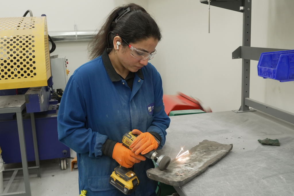 A worker uses a drill with a metal brush attachment to polish an ingot of rare earth metal known as neodymium-praseodymium oxide, Wednesday, July 22, 2026, at the Phoenix Tailings refinery in Exeter, N.H. (AP Photo/Rodrique Ngowi)