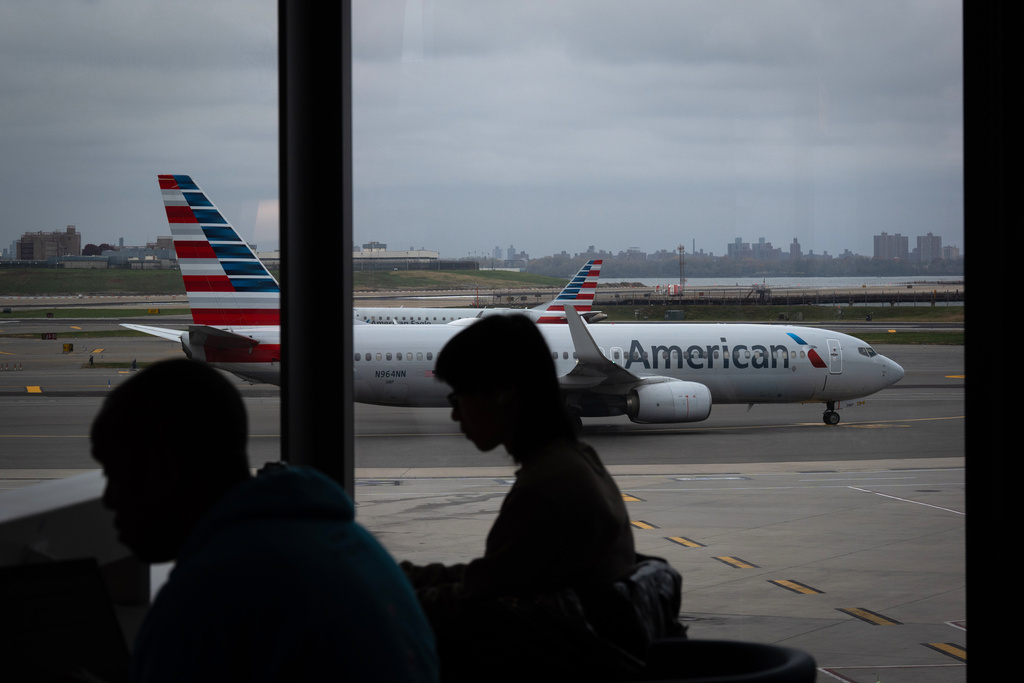 People wait for flights as an American Airlines plane taxis at LaGuardia Airport (LGA), in the Queens borough of New York, Sunday, Nov. 9, 2025. (AP Photo/Adam Gray)