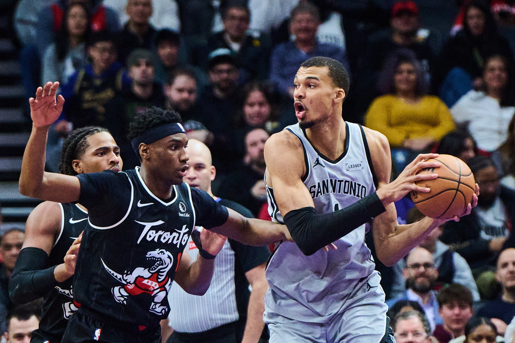 San Antonio Spurs' Victor Wembanyama (1) looks for a pass as Toronto Raptors' Ja'Kobe Walter (14) defends during the first half of an NBA basketball game, in Toronto, Wednesday, Feb. 25, 2026. (Sammy Kogan/The Canadian Press via AP)