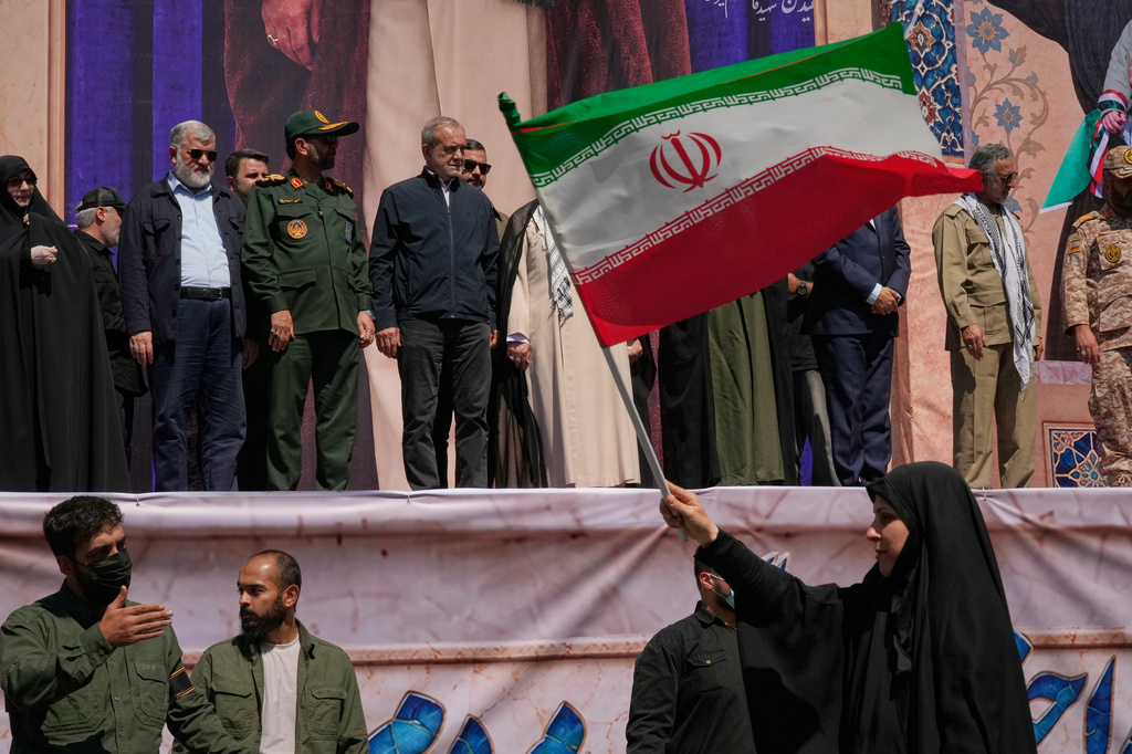 Iranian President Masoud Pezeshkian, center left, and other officials watch as a woman waves an Iranian flag during the state-organized "Janfada," or "Sacrifice for Iran," military-style parade in Tehran, Iran, Friday, Sept. 18, 2026. (AP Photo/Vahid Salemi)