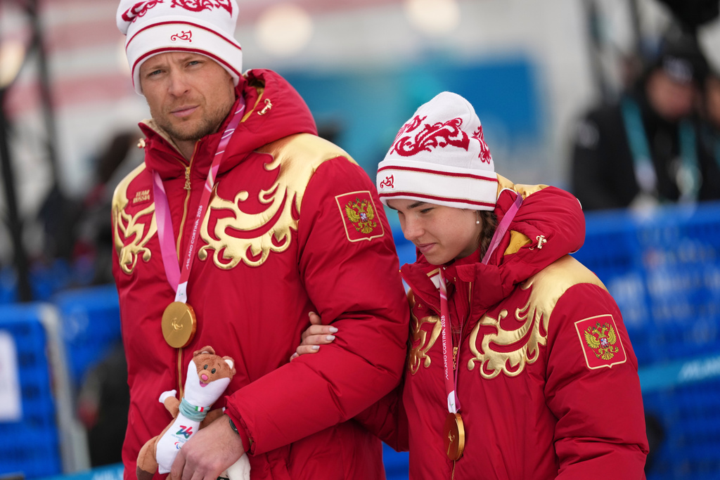 Anastasiia Bagiian, of Russia, leaves the podium with her guide Sergei Siniakin, after winning the gold medal in the cross country skiing women's 10Km interval start classic vision impaired final at the 2026 Winter Paralympics, in Tesero, Italy, Wednesday, March 11, 2026. (AP Photo/Evgeniy Maloletka)