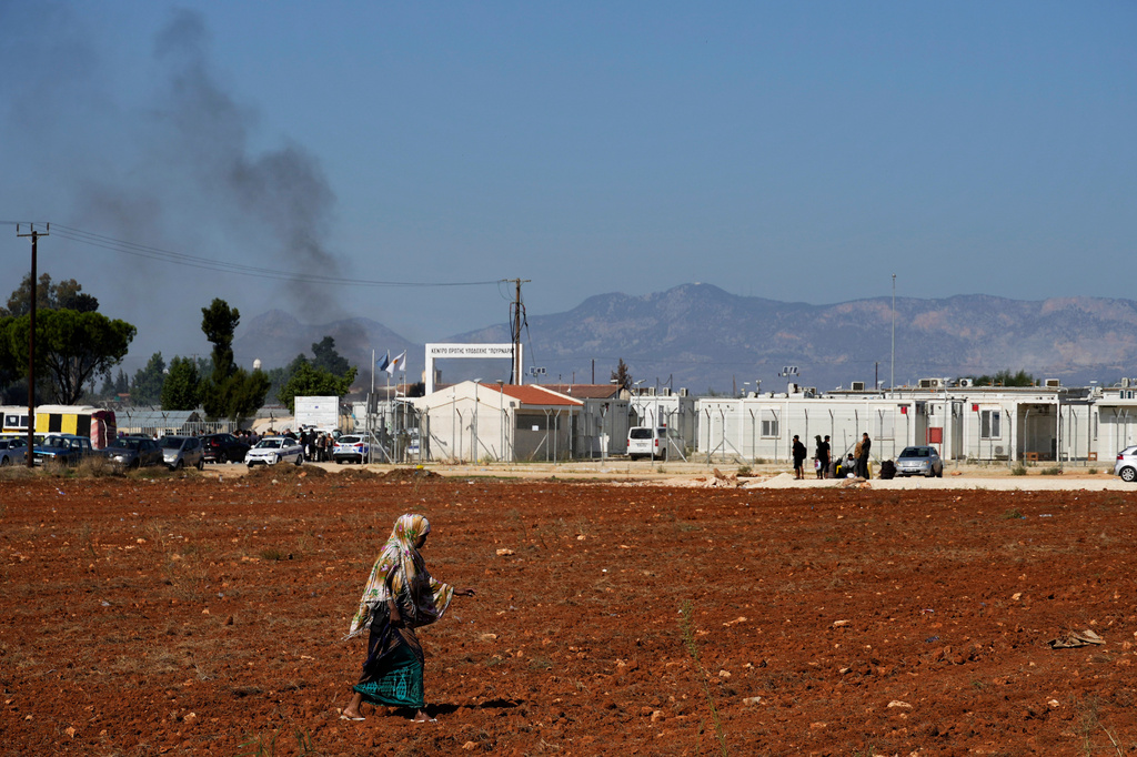 FILE - A migrant walks in a field as smoke from a fire rises from inside the Pournara migrant reception center following fighting between rival groups inside the camp near the village of Kokkinotrimithia, on the outskirts of the capital Nicosia, Cyprus, Friday, Oct. 28, 2022. (AP Photo/Petros Karadjias, File)