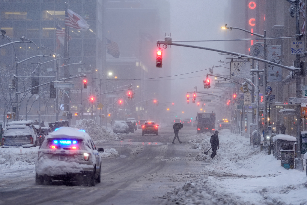 A law enforcement vehicle makes its way down Sixth Avenue as pedestrians cross during a snow storm, Monday, Feb. 23, 2026, in New York. (AP Photo/Seth Wenig)
