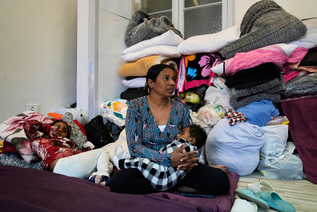 A displaced migrant woman, who among many others who fled Israeli strikes in southern and eastern Lebanon and Beirut's southern suburbs, sits with her children on mattresses at Saint Joseph Church, which has been turned into a shelter for displaced migrants, mostly from African nations, in Beirut, Wednesday, March 11, 2026. (AP Photo/Hussein Malla)
