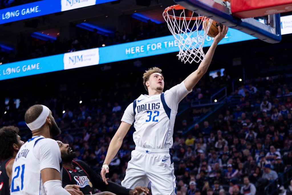 Dallas Mavericks' Cooper Flagg, right, goes up to shoot as Philadelphia 76ers' Andre Drummond, second from right, watches during the first half of an NBA basketball game, Saturday, Dec. 20, 2025, in Philadelphia. (AP Photo/Chris Szagola)