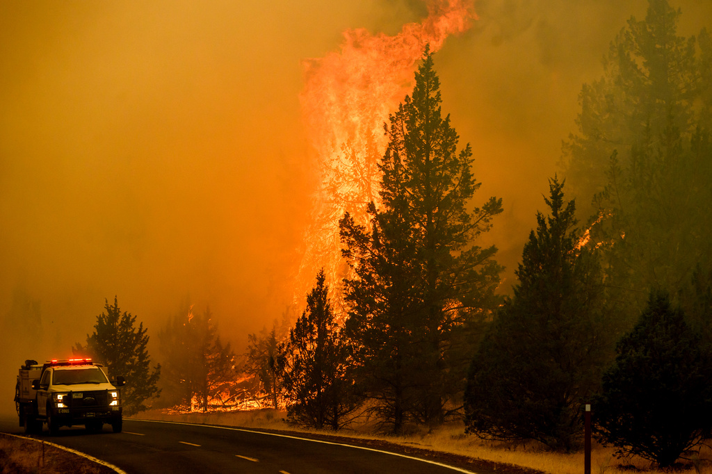 A vehicle drives along Jackson Trail Rd. as the Bench fire burns on Saturday, July 25, 2026, in Warm Springs, Ore. (AP Photo/Noah Berger)
