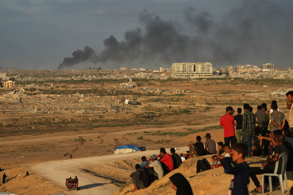 Displaced Palestinians watch smoke rise after Israeli military strikes as they gather on the coastal road near Wadi Gaza, in the central Gaza Strip, Thursday, Oct. 9, 2025. (AP Photo/Abdel Kareem Hana)