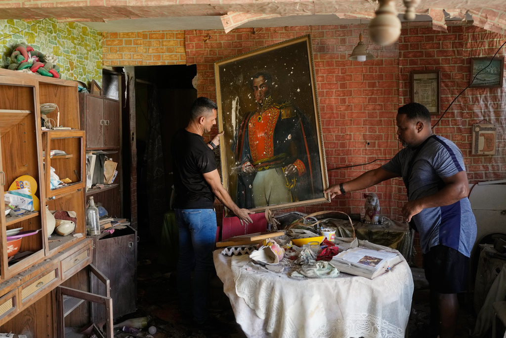 Jesus Linares, right, removes a painting of independence hero Simon Bolivar at his home, which he says was hit during U.S. military operations to capture Venezuelan President Nicolas Maduro, in Catia La Mar, Venezuela, Sunday, Jan. 4, 2026. (AP Photo/Matias Delacroix)
