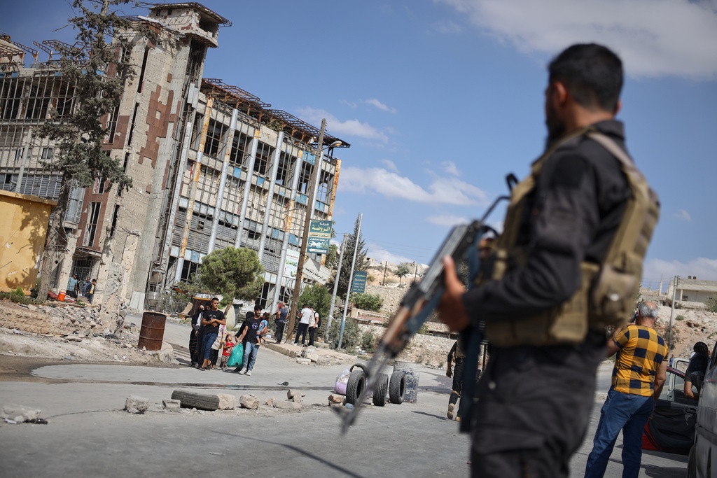 Syrian security forces stand guard as residents leave the Sheikh Maqsoud and Achrafieh neighborhoods of Aleppo, Syria, Tuesday, Oct. 7, 2025, following overnight clashes between Syrian government troops and the Kurdish-led Syrian Democratic Forces. (AP Photo/Omar Albam)