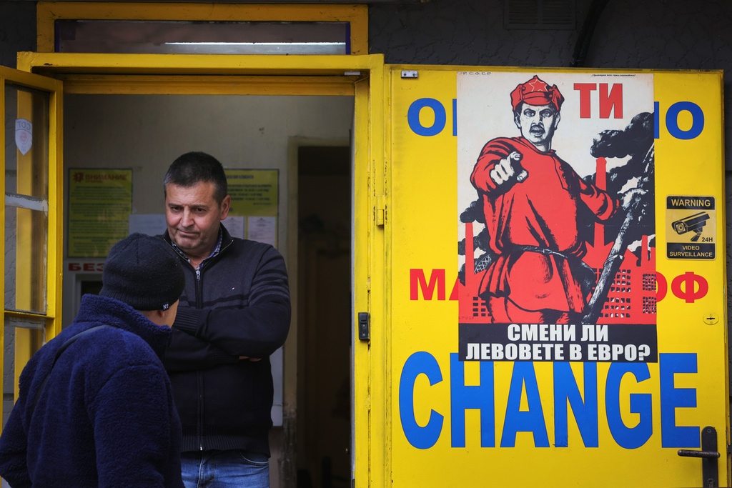People stand at a currency exchange office with a poster reading "Did you exchange your levs for euros?" in Sofia, Saturday, Dec. 27, 2025. (AP Photo/Valentina Petrova)