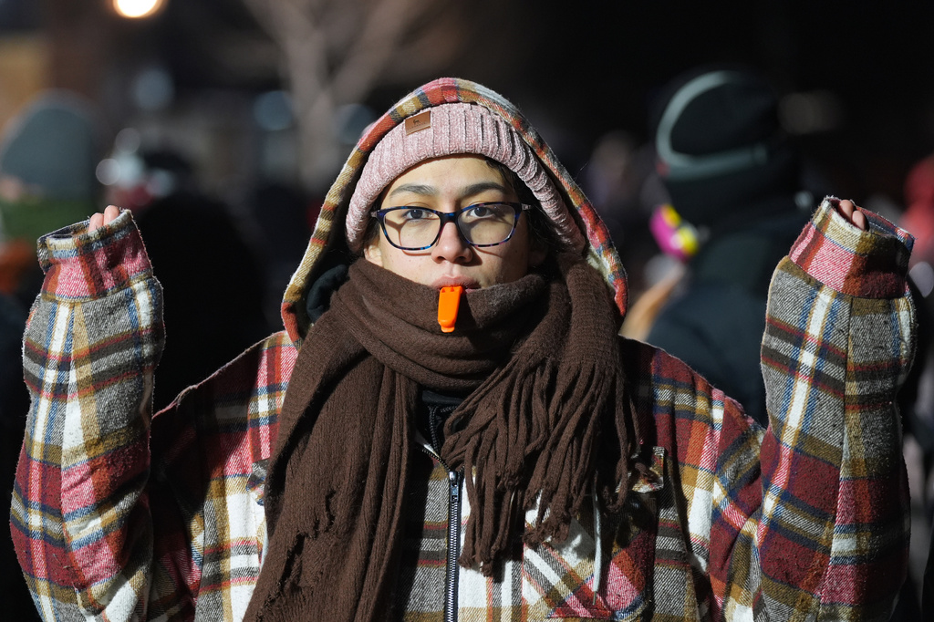 A person holds a whistle in their mouth as police face off with protesters during a noise demonstration outside the Graduate by Hilton Minneapolis hotel on Wednesday, Jan. 28, 2026, in Minneapolis. (AP Photo/Adam Gray)