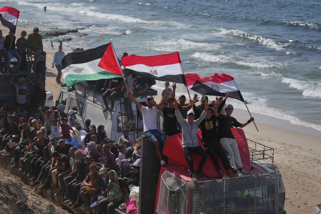 Displaced Palestinians ride on trucks loaded with belongings and wave Egyptian and Palestinian flags as they travel along the coastal road near Wadi Gaza in the central Gaza Strip, moving toward Gaza city, Saturday, Oct. 11, 2025, after Israel and Hamas agreed to a pause in their war and the release of the remaining hostages. (AP Photo/Jehad Alshrafi)