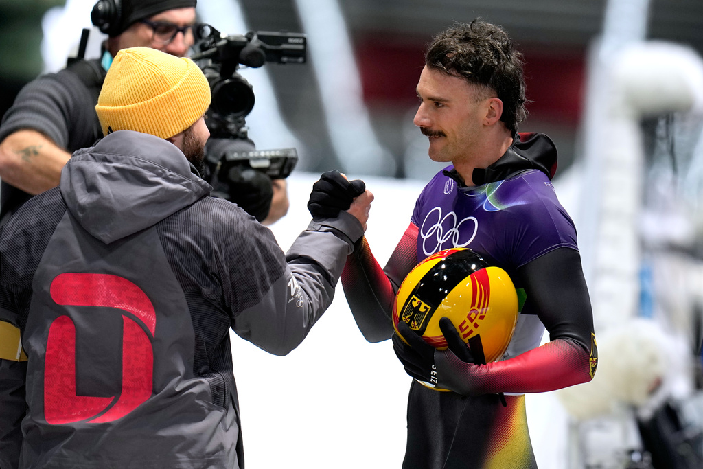 Germany's Axel Jungk, right, arrives at the finish during a men's skeleton run at the 2026 Winter Olympics, in Cortina d'Ampezzo, Italy, Thursday, Feb. 12, 2026. (AP Photo/Alessandra Tarantino)