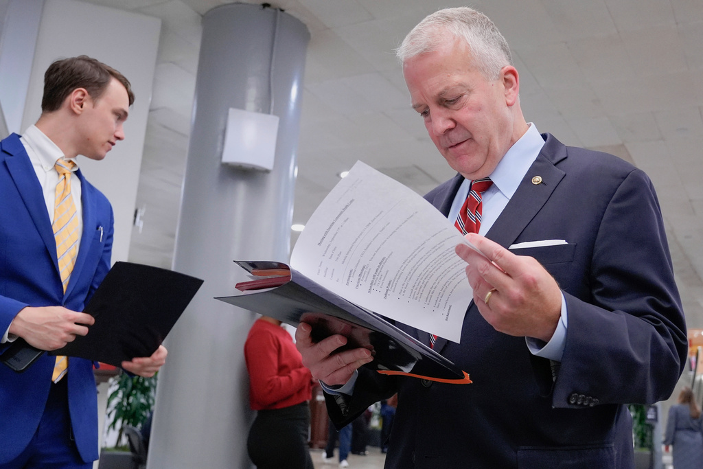 Sen. Dan Sullivan, R-Alaska, right, reads documents at the Capitol subway, Wednesday, Sept. 17, 2025, in Washington. (AP Photo/Mariam Zuhaib)