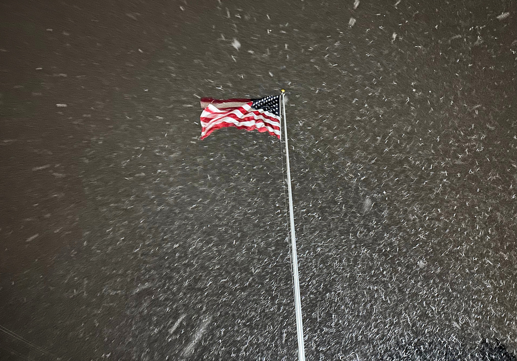 A flag ripples in the wind as snow falls in Lowville, New York, on Tuesday night, Dec. 9, 2025. The area faces a winter storm warning through Thursday. (AP Photo/Cara Anna)