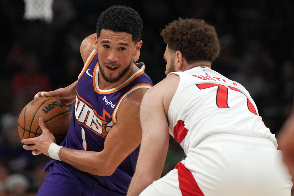 Phoenix Suns guard Devin Booker shields the ball from Toronto Raptors forward Jamison Battle (77) during the first half of an NBA basketball game, Sunday, March 23, 2026, in Phoenix. (AP Photo/Rick Scuteri)