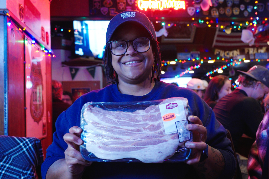 In this image made from video, Ashley Burris holds up a pack of bacon she won during a meat raffle at the 1029 Bar in Minneapolis, April 3, 2026. (AP Photo/Mark Vancleave)