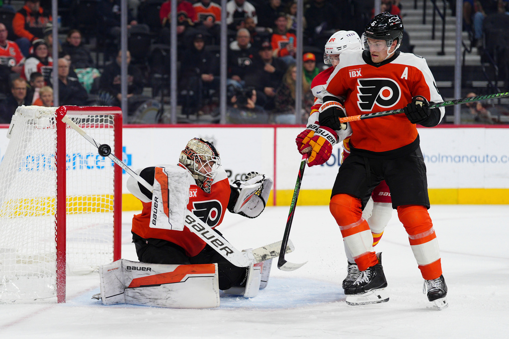 Philadelphia Flyers goaltender Aleksei Kolosov, left, makes a save past Travis Sanheim (6) and Calgary Flames' Joel Farabee, rear, during the first period of an NHL hockey game, Sunday, Nov. 2, 2025, in Philadelphia. (AP Photo/Derik Hamilton)