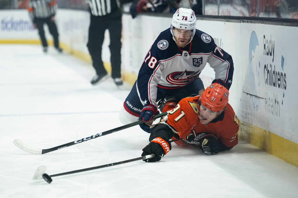 Anaheim Ducks center Leo Carlsson (91) reaches for the puck as Columbus Blue Jackets defenseman Damon Severson (78) checks him during the first period of an NHL hockey game, Saturday, Dec. 20, 2025, in Anaheim, Calif. (AP Photo/Kyusung Gong)