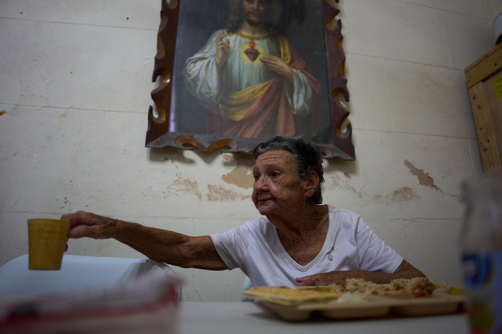 Mercedes Lopez Rey, 83, holds out her cup to be filled with water in a dining hall adjacent to the Church of the Holy Spirit, where a church-run program provides free meals to seniors three times a week, in Old Havana, Cuba, Friday, April 10, 2026. (AP Photo/Ramon Espinosa)