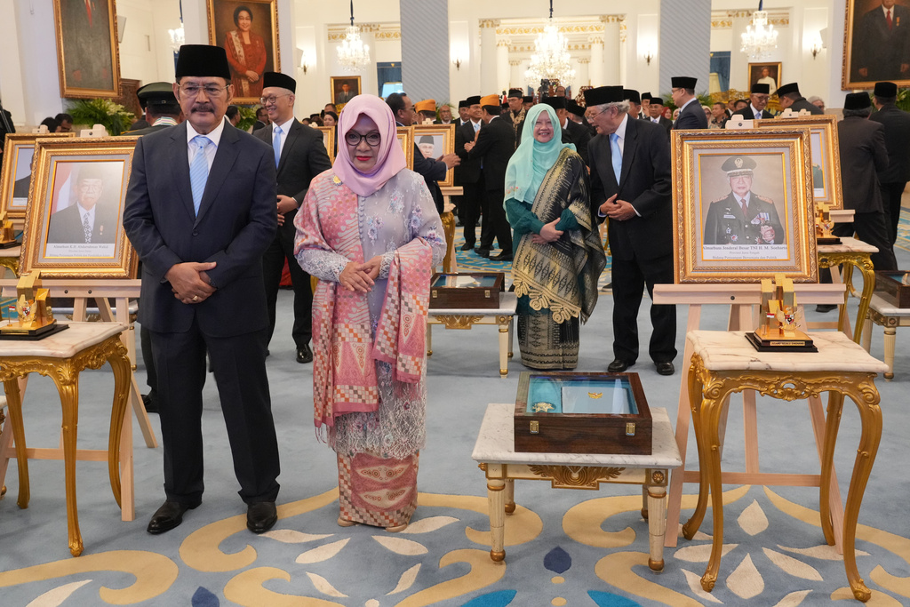 Siti Hardiyanti Rukmana, second left, daughter of the late President Suharto and son Bambang Trihatmojo, left, pose for photographers next to the portrait of their father during a ceremony awarding national hero title to ten figures including the former strongman, at the State Palace in Jakarta, Indonesia, Monday, Nov. 10, 2025. (AP Photo/Achmad Ibrahim)