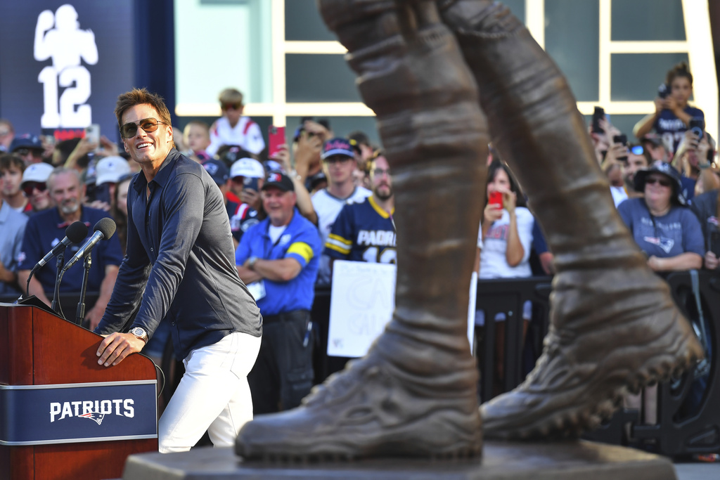 Former New England Patriots quarterback Tom Brady, left, looks at a bronze statue of himself after it was unveiled in Patriot Place Plaza before an NFL preseason football game between the Washington Commanders and the New England Patriots Friday, Aug. 8, 2025, in Foxborough, Mass. (AP Photo/Charles Krupa)