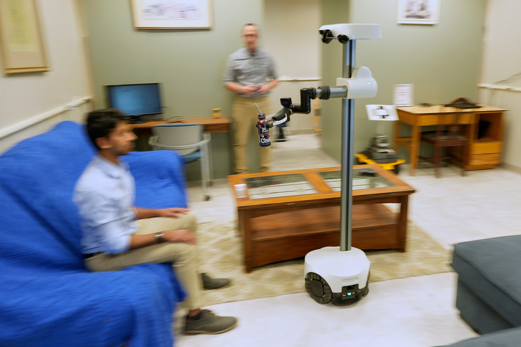 A robot operated by a robotics engineer, rear, brings a drink to colleague during a demonstration at the University of New Hampshire, Tuesday, April 21, 2026, in Durham, N.H. (AP Photo/Robert F. Bukaty)