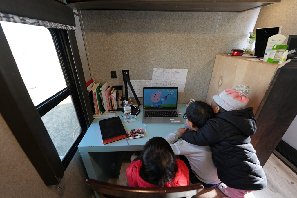 Siblings Mo Songhua, left, Mo Songen, center, and Mo Nika, right, from the Mayflower Church community watch, "Peppa Pig," to strengthen their English, inside their family's trailer in Midland, Texas, Jan. 20, 2025. (AP Photo/Rebecca Blackwell)