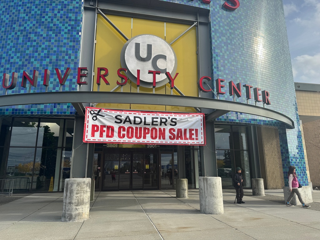 A sign advertising a sale related to the issuance of Alaska Permanent Fund Dividend, or PFD, checks hangs outside a mall entrance in Anchorage, Alaska, Tuesday, Sept. 23, 2025. (AP Photo/Mark Thiessen)
