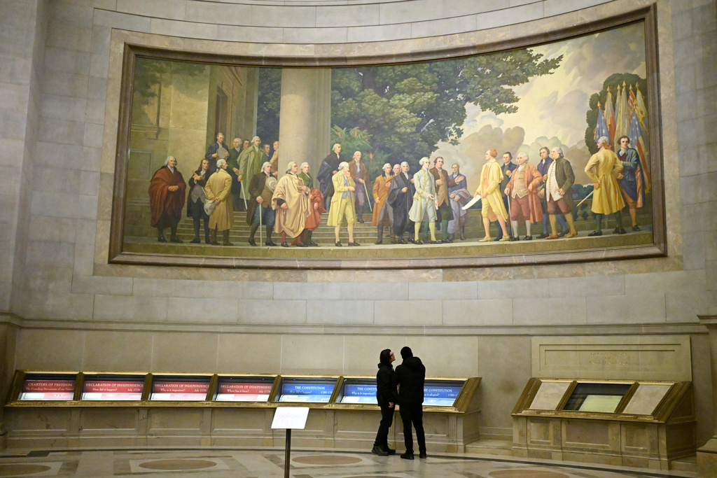 Two visitors look at exhibits beneath a large wall mural showing the signing of the Declaration of Independence at the National Archives Thursday, Jan. 29, 2026, in Washington. (AP Photo/John McDonnell)