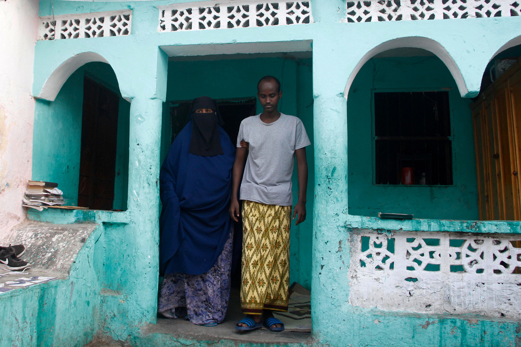 Mohamed Abdi Awale, who says he was tortured by smugglers while trying to reach Europe, is helped by his mother at their home in Mogadishu, Somalia, Monday, Nov. 17, 2025. (AP Photo/Farah Abdi Warsameh)