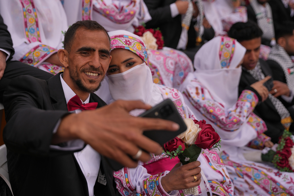 A Palestinian couple poses for a selfie as they get married in a mass wedding ceremony in Deir al-Balah, central Gaza Strip, Friday, April 24, 2026. (AP Photo/Abdel Kareem Hana)