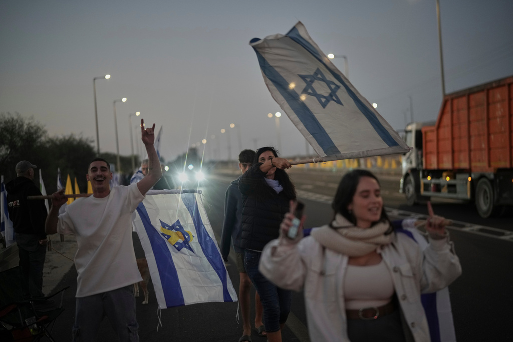 People hold Israeli flags as they gather prior to the release of Israeli hostages held in Gaza, in front of a military base near Reim Area, southern Israel, on Monday, Oct, 13, 2025. (AP Photo/Leo Correa)