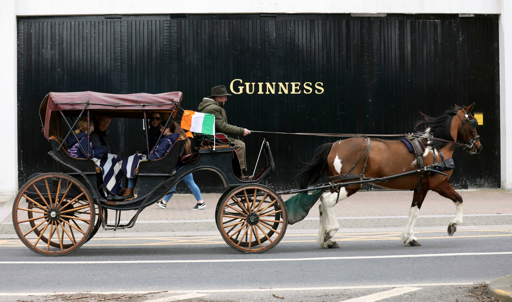 FILE - Tourists in a horse and cart pass the Guinness factory in Dublin city center, March, 16, 2020. (AP Photo/Peter Morrison, File)