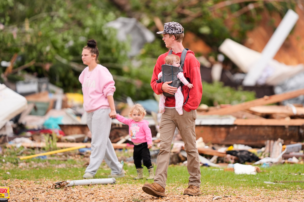 Jordyn Coleman, left, and Dennis Menard walk with their children among debris at Gene's Mobile Home Supply, a trailer park in Bogue Chitto, Miss., Thursday, May, 7, 2026, after a tornado cut across the state. (AP Photo/Gerald Herbert)